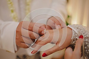 A photo of a male couple inserting a ring into a woman`s finger