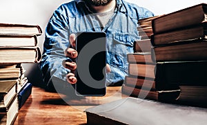 Photo of male person holding smartphone amidst old books