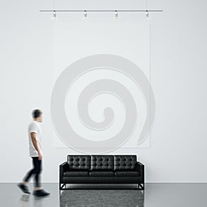 Photo of man in gallery. Waching empty canvas hanging on the brick wall and black generic design sofa concrete floor