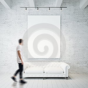 Photo of man in gallery. Waching empty canvas hanging on the brick wall and vintage classic sofa wood floor. Square