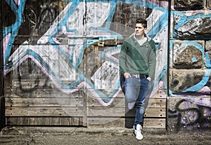 Photo of a man leaning against a graffiti-covered wall