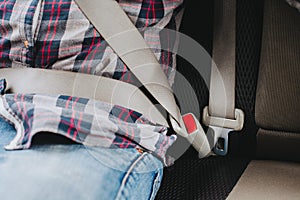 Photo of man in plaid shirt sitting in a car putting on seat belt