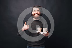 A photo of a man smiling at the camera and holding two cups of hot drinks being thankful for their quality