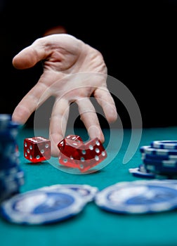 Photo of man throwing red dice on table with chips in casino