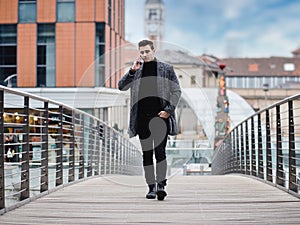 Photo of a man walking across a bridge while talking on a cell phone