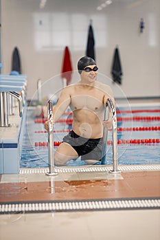Asian man in hat and goggles getting out of swimming pool by the ladder photo
