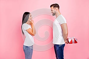 Photo of man wearing t-shirt hiding present behind back intending to gift his astonished amazed girl wearing jeans denim