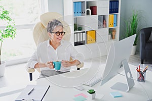 Photo mature age boss business worker woman gray hair hold her cup fresh coffee watch monitor desktop news isolated on