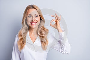 Photo of mature attractive charming smiling positive woman doctor showing okay sign isolated on grey color background