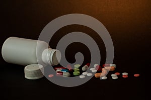 Photo of medicinal pills outside a white bottle photographed against a dark background