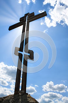 Photo of a metal orthodox cross close-up in projection against a blue sky with clouds and a bright sun glare cross