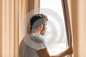 Photo of middle age bearded man looking in the window in the morning.