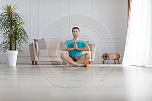 Photo of a middle aged man at home. He sits in the lotus position with headphones and listens to meditation music.