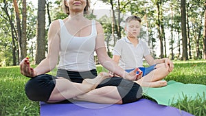 Photo of middle aged mother with her teenage boy child doing yoga and breathing exercises at park. Family taking care of