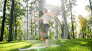 Photo of middle aged smiling woman practicing yoga and meditating at park. Woman stretching and doing fitness on mat at