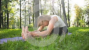 Photo of middle aged smiling woman practicing yoga and meditating at park. Woman stretching and doing fitness on mat at