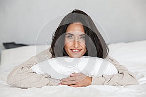 Photo of middle-aged woman 30s smiling, while lying in bed with white linen at home