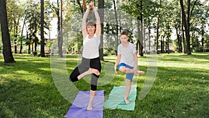 Photo of middle aged woman teaching her student in yoga class at park. Woamn with teenage boy practising fitness