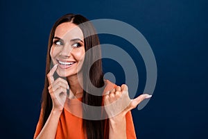 Photo of minded gorgeous woman dressed orange t-shirt indicating look at stomatology ad empty space isolated on dark