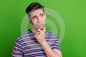 Photo of minded suspicious guy with stubble dressed striped t-shirt thoughtfully look empty space isolated on green