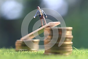 Miniature figure young bussinesman keep trying to get higher income walking at stack of coin at fresh green grass in the morning