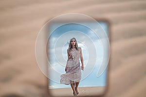 Photo in the mirror of attractive blond woman in long dress walking in desert