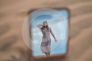 Photo in the mirror of attractive blond woman in long dress walking in desert