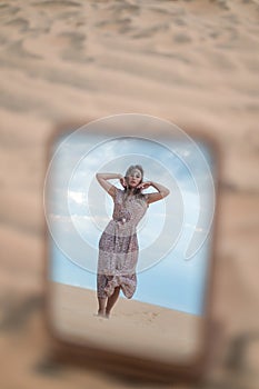 Photo in the mirror of attractive blond woman in long dress walking in desert