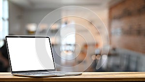 Photo of modern laptop with white blank screen display setting on the wooden table.