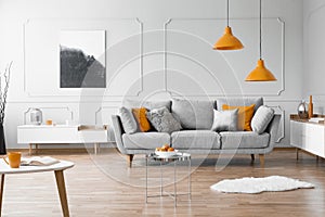 Photo of a modern living room interior with a sofa, orange lamps and painting