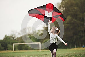 Photo in motion. Happy girl in casual clothes running with kite in the field. Beautiful nature