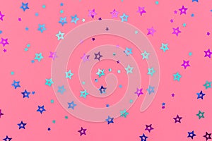 Photo of multi-colored stars glitter sprinkles on pink background. Festive holiday background for your projects. Celebration