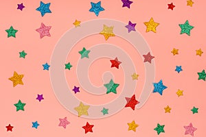 Photo of multi-colored stars glitter sprinkles on pink trendy background. Festive holiday background for your projects.