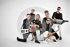 Photo of multi ethnic music band in studio.Musicians and woman soloist posing over white background