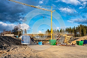 Photo of new bridge building site with timbering construction for further filling it with concrete. Yellow crane tower, blue