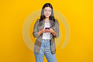 Photo of nice adorable positive woman straight hairdo wear gray shirt hold smartphone typing sms isolated on yellow