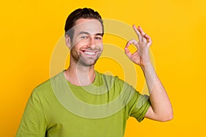 Photo of nice brunet hairdo young guy show okey wear green t-shirt isolated on bright yellow color background