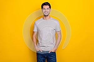 Photo of nice brunet millennial guy wear grey t-shirt jeans isolated on yellow color background