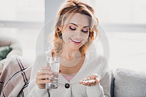 Photo of nice cheerful person sit couch arm hold vitamin pills glass fresh water comfy atmosphere flat indoors