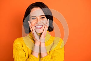Photo of nice cute toothily smiling girl holding her cheeks showing her cuteness while isolated with orange background