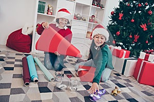 Photo of nice dreamy kids wrap paper package santa workshop concept wear x-mas hat jumper in decorated home indoors