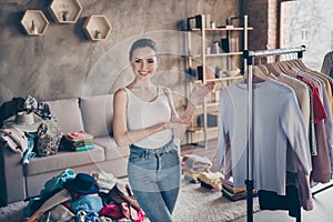 Photo of nice lovely happy girl wearing denim jeans standing showing her design collection of clothes in new flat house.