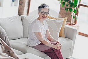 Photo of nice senior woman sit sofa enjoy weekend dressed white clothes cozy living room home house flat indoors pension