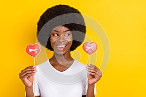 Photo of nice young happy dark skin woman look empty space hold heart candy isolated on yellow color background