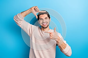 Photo of nice young man fingers make cadre symbol wear beige sweatshirt isolated on blue color background