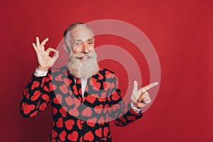 Photo of old man finger indicate empty space show okey sign wear heart print suit isolated red background