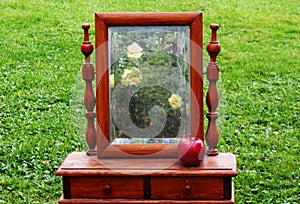 Photo of an old table mirror in a wooden frame on the green grass background