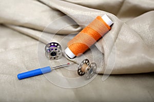 Photo of one orange thread, needle ripper and bobbin on the cloth