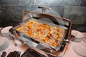 Photo of open steel Bain Marie on stand with a dish of Italian cuisine - pasta with tomato Basil and minced beef meat