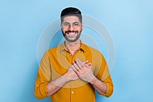 Photo of optimistic carefree dreamy guy in glasses put hands on chest feel grateful thankful charity isolated on blue